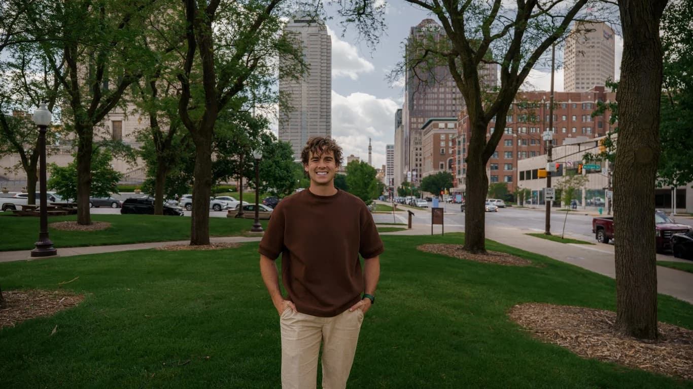 Ian DeFelice standing in a downtown Indianapolis park with the city skyline behind him